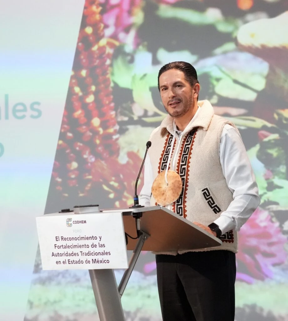 El presidente de la CODHEM Víctor Leopoldo Delgado Pérez encabeza el Foro “El Reconocimiento y Fortalecimiento de las Autoridades Tradicionales en el Estado de México”, como parte de las acciones para fortalecer los derechos de los pueblos indígenas y visibilizar su legado cultural. En la imagen se encuentra en un podio durante su intervención, portando indumentaria con elementos tradicionales que resaltan el simbolismo cultural promovido por la nueva imagen institucional de la CODHEM.