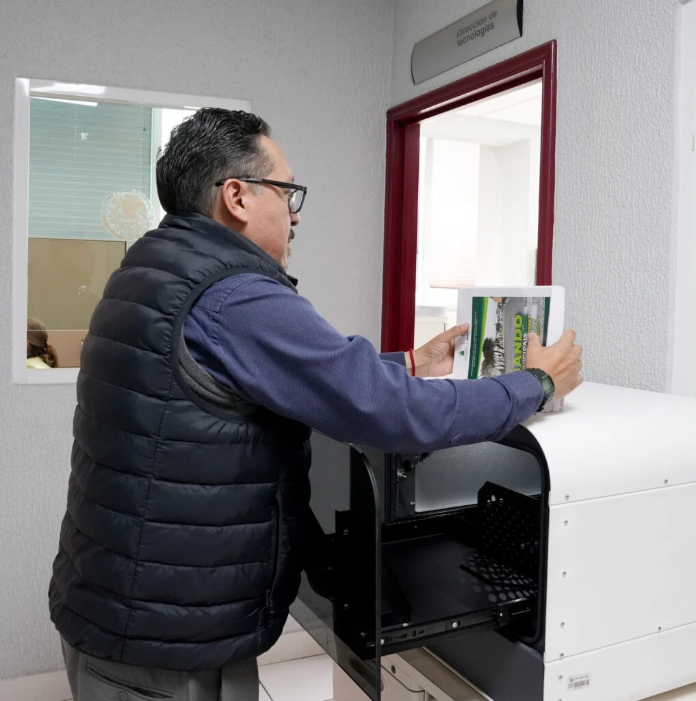 Persona coloca un ejemplar del Bando Municipal de Zinacantepec en una impresora braille dentro de un área de trabajo de la CODHEM, como parte del proceso de impresión en braille de los bandos municipales de Metepec y Zinacantepec.