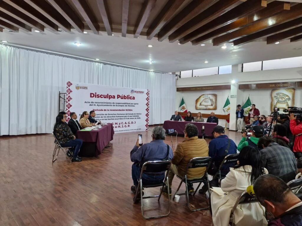 Acto público realizado en un recinto municipal, con la participación de autoridades, personas asistentes y medios de comunicación. Al frente se observa una mampara con el texto “Disculpa Pública”, mientras se desarrolla una ceremonia institucional relacionada con el reconocimiento de responsabilidades por parte de una autoridad municipal. La imagen documenta una actividad vinculada a la defensa y promoción de los derechos humanos en el Estado de México.