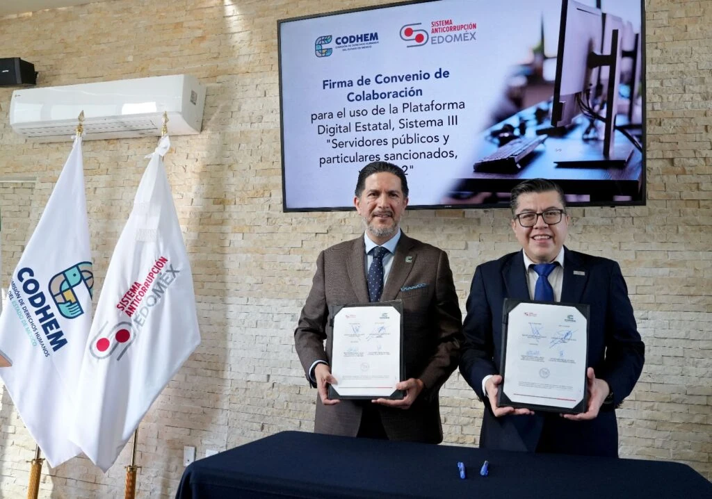 Representantes de la CODHEM y del SESAEMM muestran documentos firmados durante el convenio de colaboración para prevenir la corrupción, con banderas institucionales y una pantalla que anuncia el uso de la Plataforma Digital Estatal al fondo.