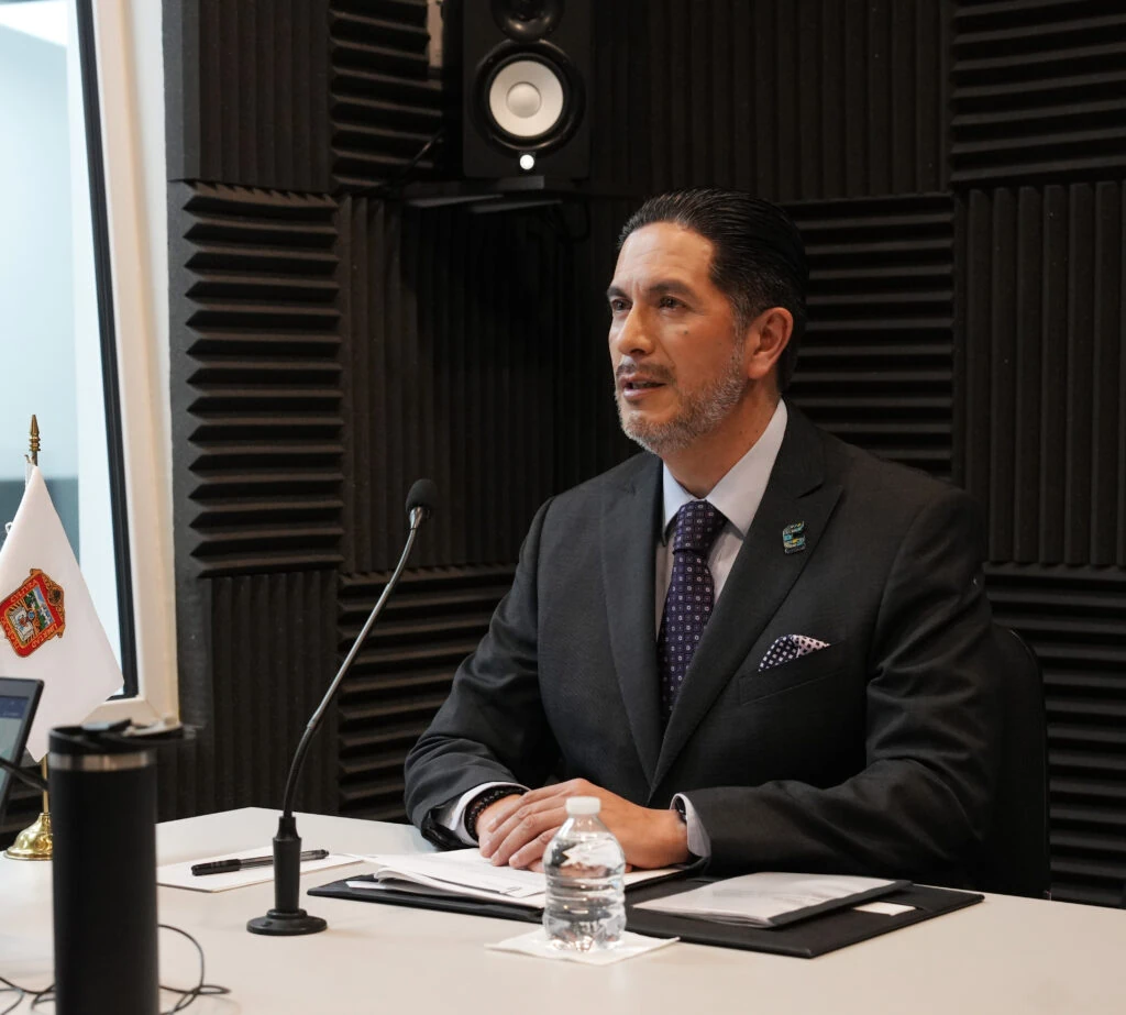 El Presidente de la Comisión de Derechos Humanos del Estado de México, Víctor Leopoldo Delgado Pérez, participa en una entrevista dentro de una cabina de grabación, con micrófono, documentos y equipo de audio sobre la mesa, donde afirmó que la CODHEM es un organismo vivo, dinámico y en constante evolución, de la sociedad y para la sociedad.
