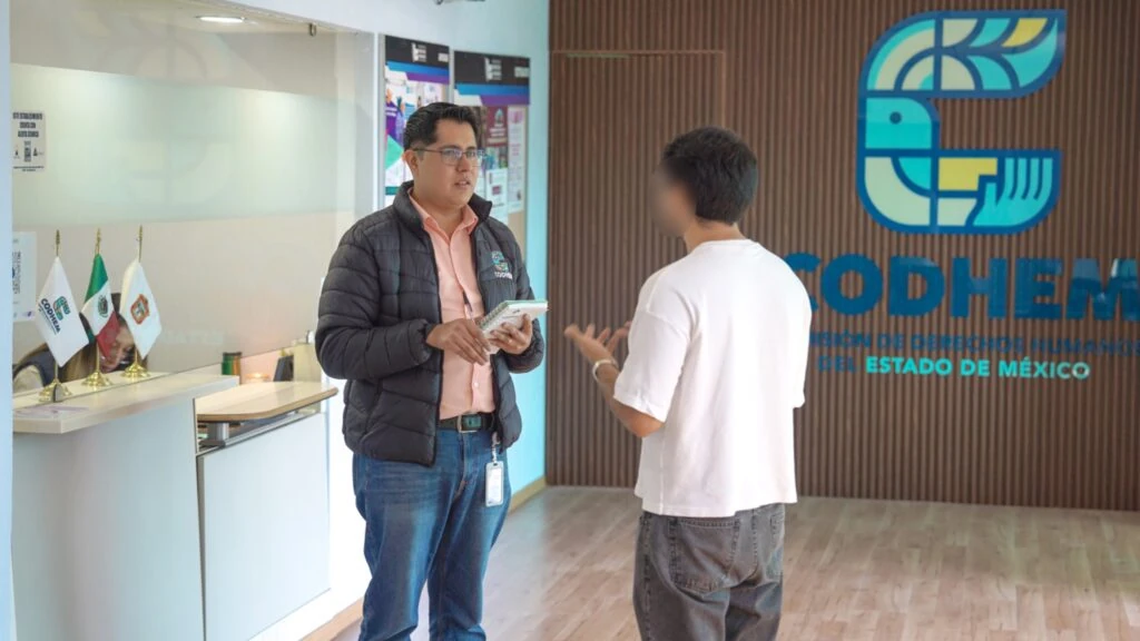 Personal de la CODHEM atiende a una persona en un área institucional con el logotipo de la Comisión de Derechos Humanos del Estado de México al fondo.