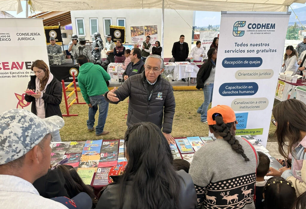 Personal de la CODHEM brinda información a personas asistentes en un módulo instalado bajo una carpa, con material impreso sobre derechos humanos y un banner institucional que indica que todos los servicios son gratuitos.