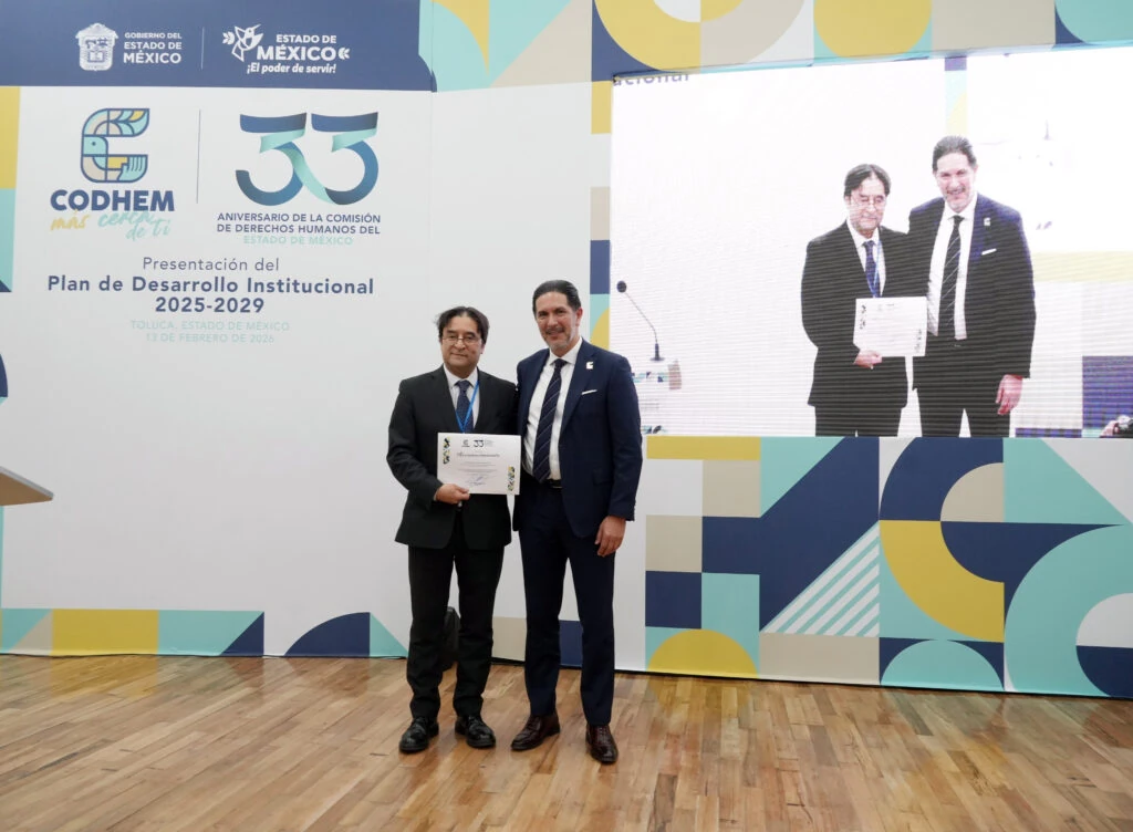 El presidente de la CODHEM Víctor Leopoldo Delgado Pérez participa en una ceremonia institucional junto a una persona que sostiene un reconocimiento, durante un evento conmemorativo de la Comisión de Derechos Humanos del Estado de México. La visita del alto comisionado Volker Türk reafirma la relevancia de México en la agenda internacional de derechos humanos.