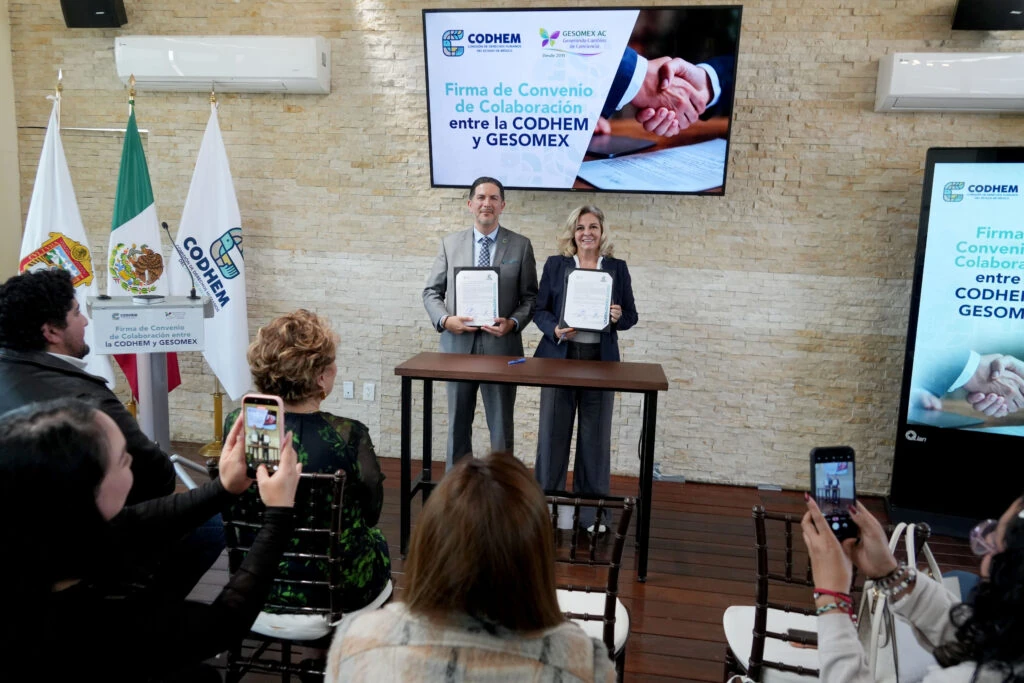 Personas participantes en la firma de convenio de colaboración entre la CODHEM y GESOMEX muestran documentos firmados frente a una audiencia; el acto institucional destaca la corresponsabilidad entre Estado y sociedad civil para reconocer, garantizar y construir la defensa de la dignidad humana.