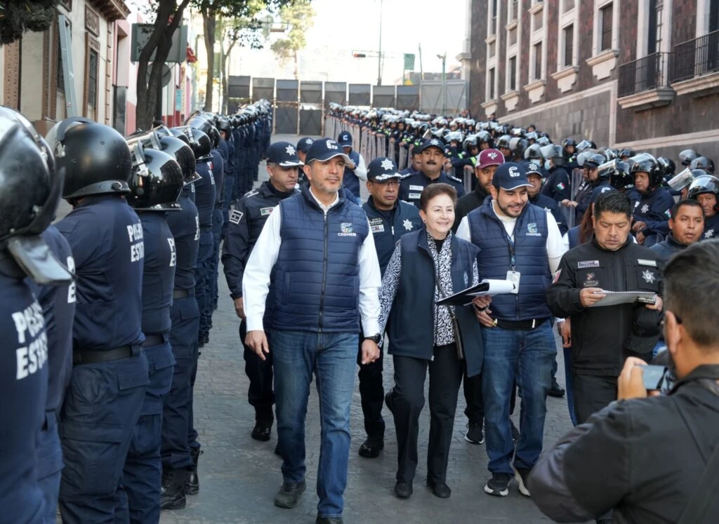 Comitiva de la CODHEM avanza entre filas de personas servidoras públicas de seguridad durante una jornada de verificación en la entidad, para constatar que no se porten armas u objetos que representen riesgo para personas manifestantes.
