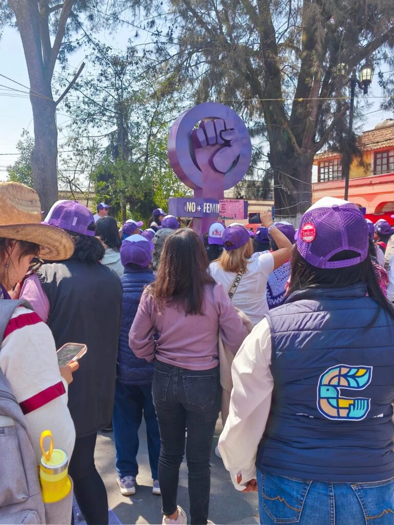 Personal de la CODHEM se encuentra entre participantes de una manifestación del 8M junto a un símbolo alusivo a la lucha por los derechos de las mujeres, como parte del acompañamiento institucional a la jornada.