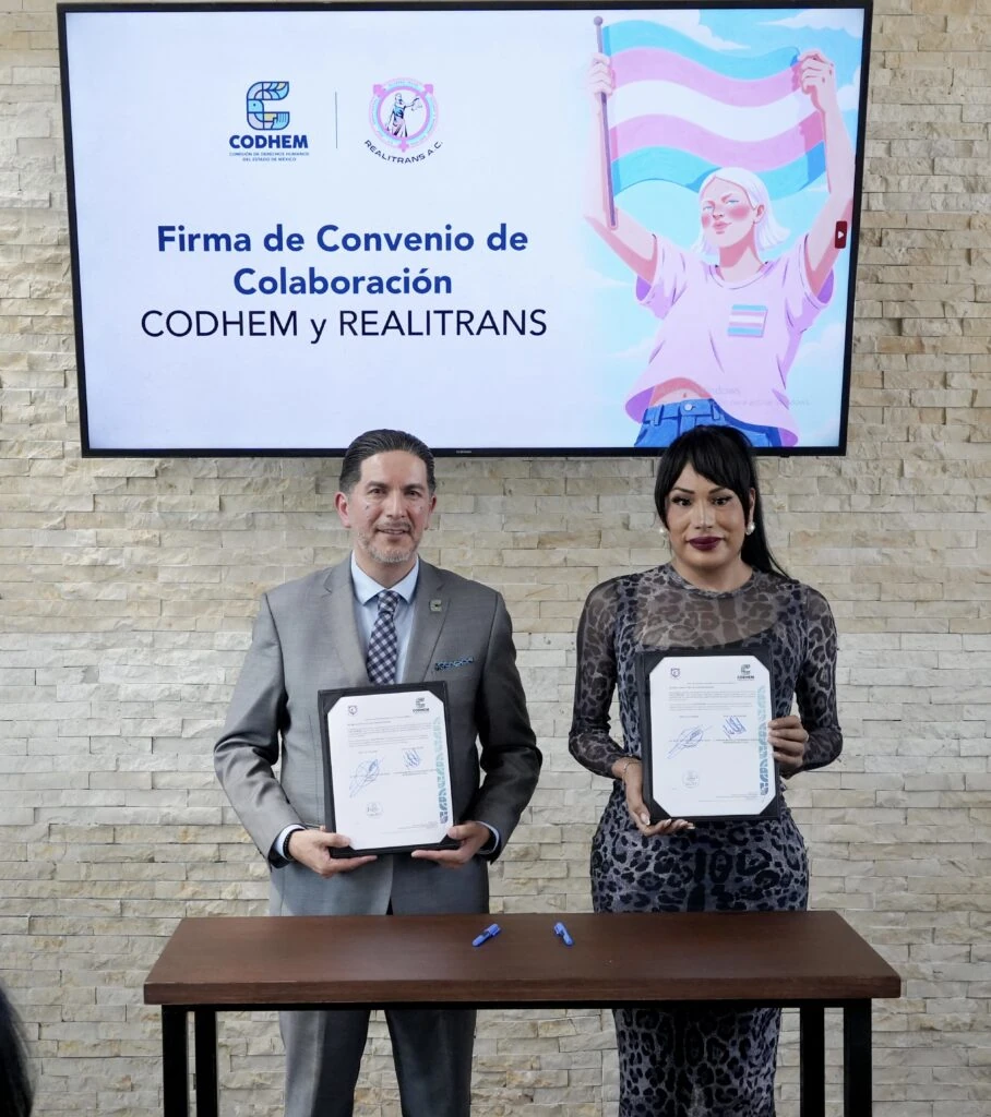Representantes de la CODHEM y de la asociación civil REALITRANS muestran los documentos firmados durante un convenio de colaboración. Al fondo se observa una pantalla con los logotipos de ambas instituciones y la leyenda “Firma de Convenio de Colaboración CODHEM y REALITRANS”, en una acción orientada a fortalecer la promoción y protección de los derechos humanos de la población LGBTTTIQ+ y de la diversidad sexogenérica.