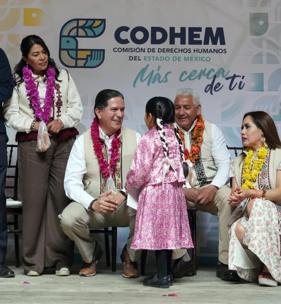 Infancia indígena con vestido tradicional participa frente a personas representantes y asistentes durante una actividad de la CODHEM, con el fondo institucional “Más cerca de ti”. La imagen enfatiza el reconocimiento del respeto, la igualdad y la dignidad de infancias y adolescencias indígenas en espacios de diálogo y participación.