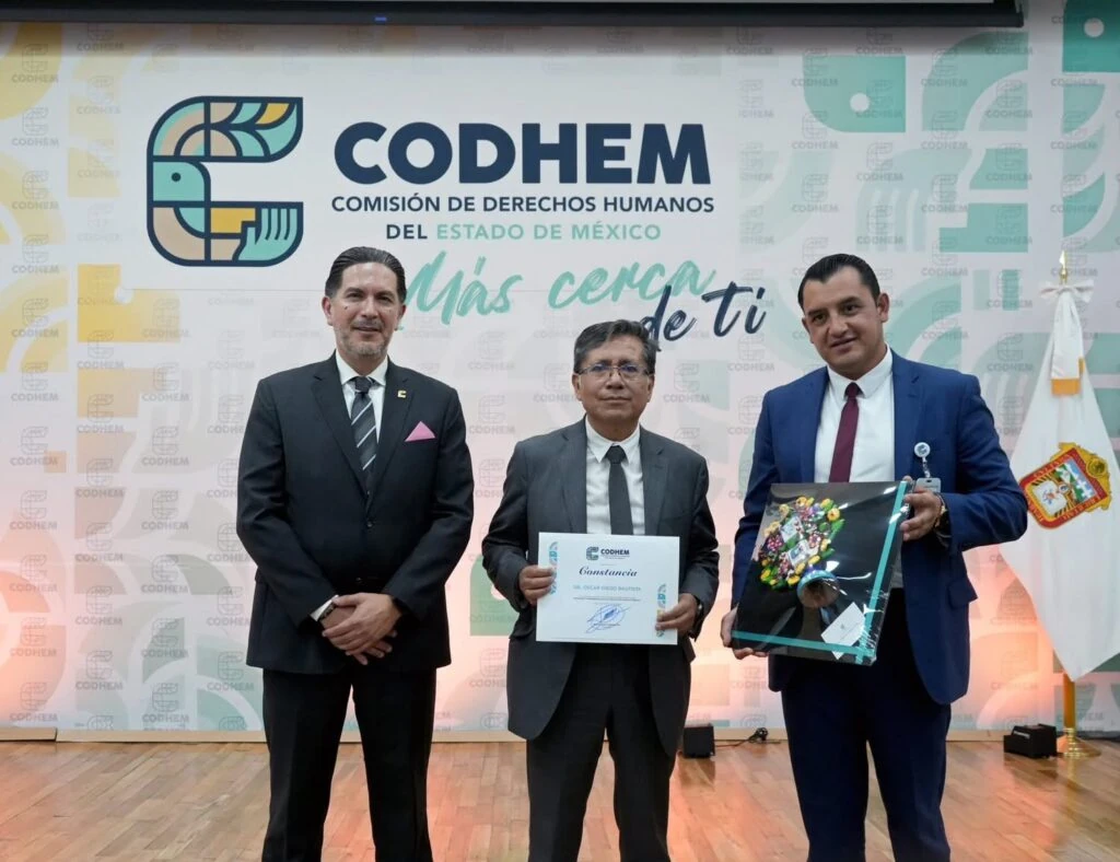 Tres personas posan en un espacio institucional de la Comisión de Derechos Humanos del Estado de México, CODHEM, frente al mural con el logotipo oficial y la frase “Más cerca de ti”. Una de las personas sostiene una constancia y otra muestra un reconocimiento, en el marco de una actividad orientada a fortalecer la cultura de ética e integridad en el servicio público. Durante el acto de bienvenida, el presidente de la CODHEM, Víctor Leopoldo Delgado Pérez, agradeció al Dr. Adrián Ociel Millán Vargas, titular del Órgano Interno de Control, por hacer posible esta actividad.