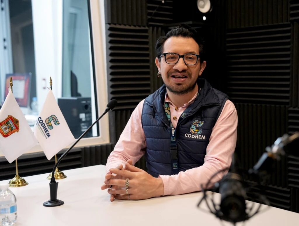 Persona participante en la grabación de un episodio de podcast en un estudio de audio de la Comisión de Derechos Humanos del Estado de México (CODHEM). La imagen muestra un espacio equipado con micrófonos, paneles acústicos y banderas institucionales, utilizado para la difusión de contenidos sobre derechos humanos, formación y sensibilización dirigidos a la ciudadanía.