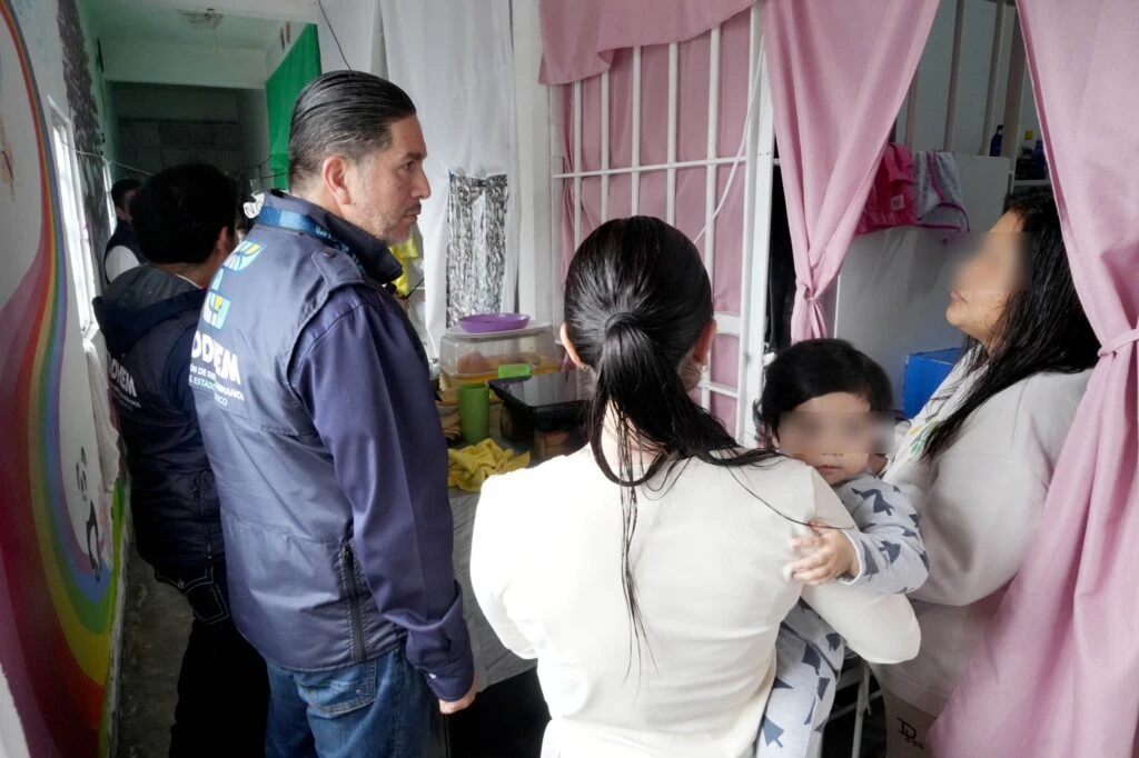 Personal de CODHEM conversa con personas dentro de una estancia, junto a una entrada con cortinas rosas.